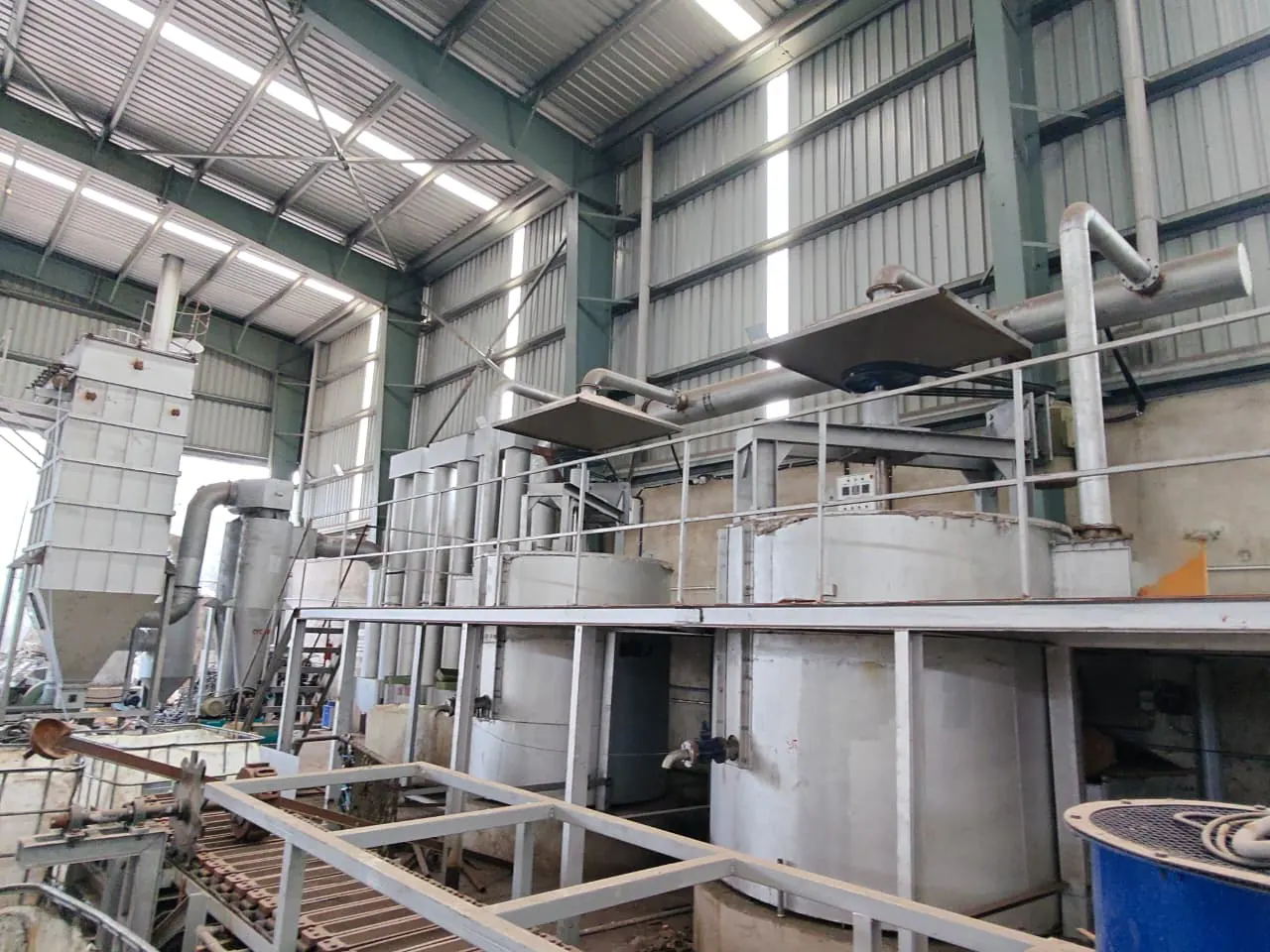 Two process vessels below a raised platform with extraction hoods, ducts, a conveyor and pollution-control equipment