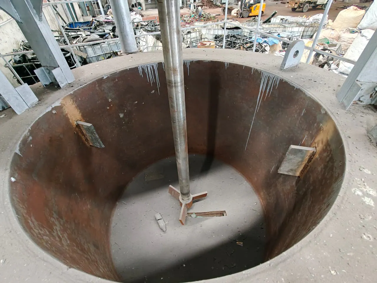Top-down view inside a cylindrical steel vessel showing its central agitator shaft, paddle and wall baffles