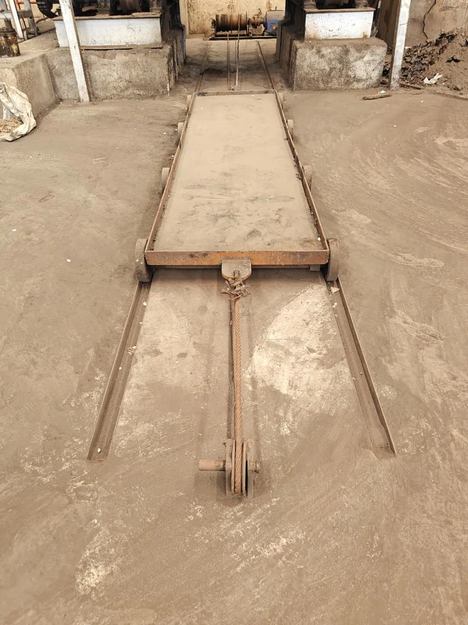 Flat industrial material trolley positioned on floor rails with a wire-rope connection