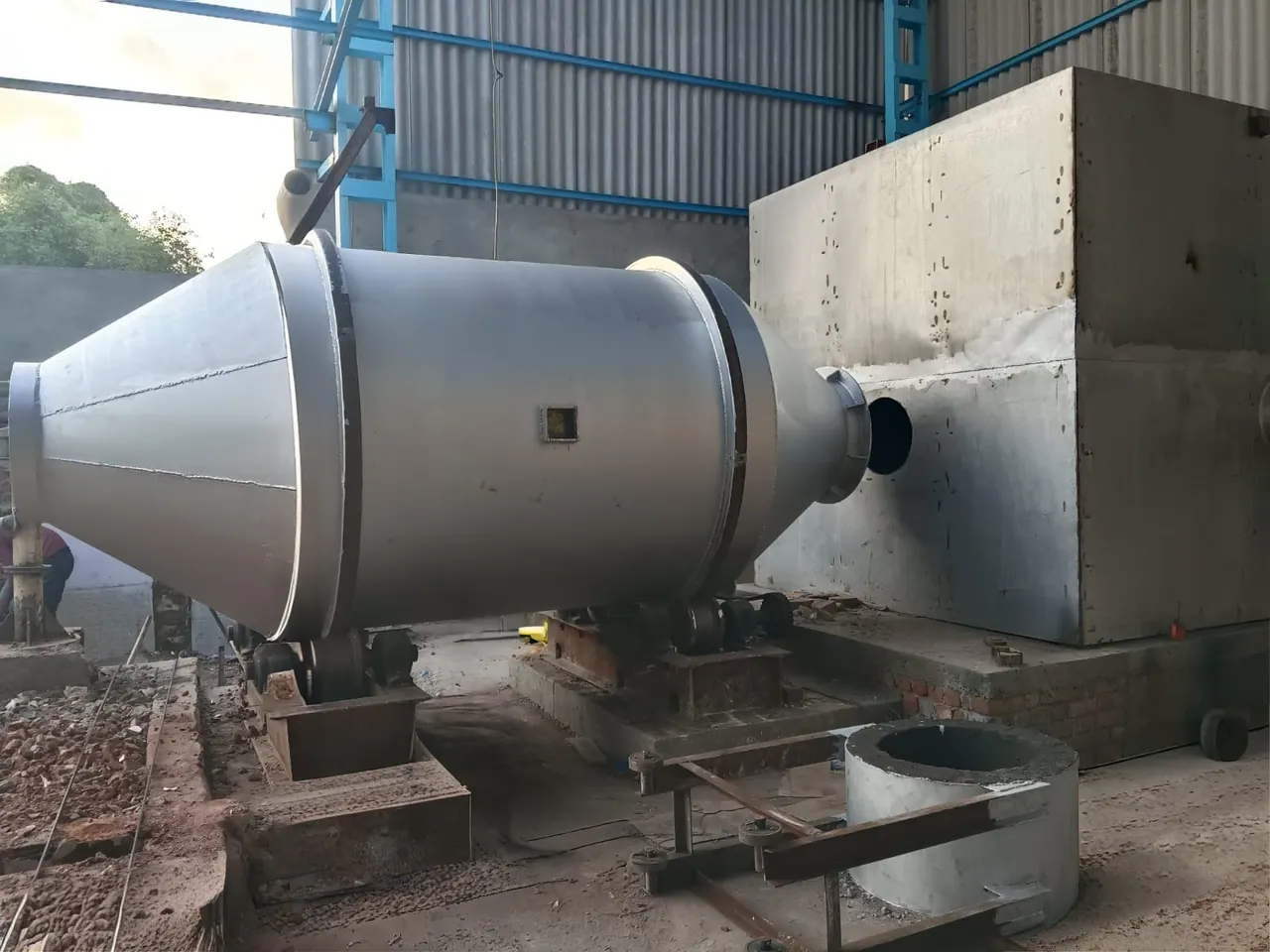 Side view of a fabricated three-ton rotary furnace connected to a large rectangular chamber